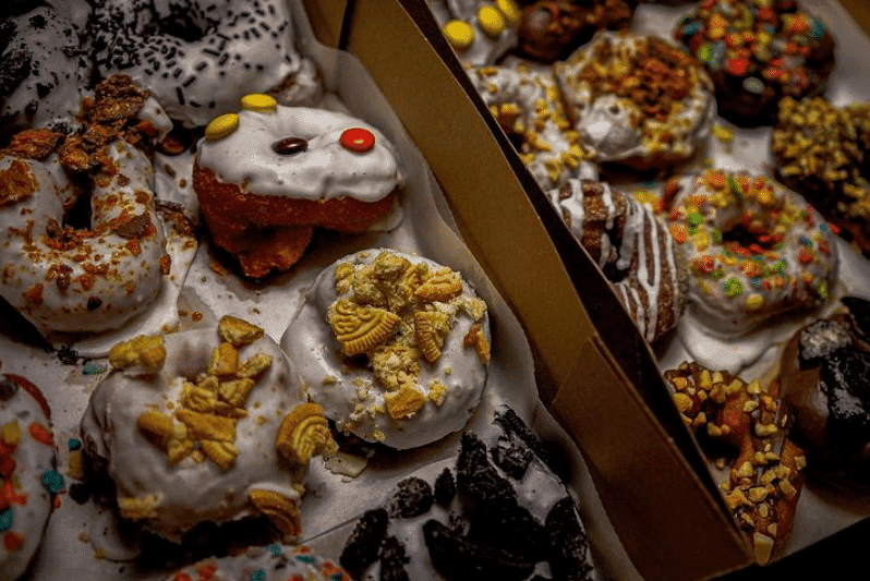 Assorted colorful donuts with various toppings displayed in open cardboard boxes.