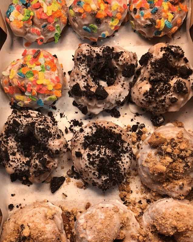 Assorted donuts topped with colorful cereal, crushed cookies, and crumbled graham crackers.