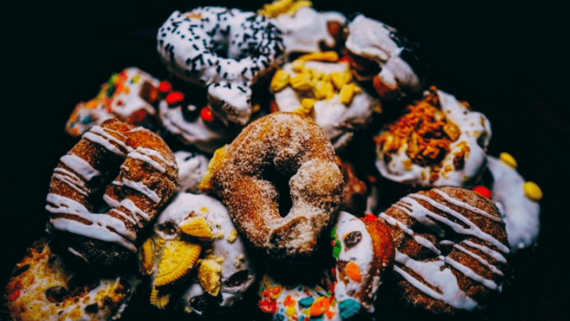 A variety of colorful, decorated donuts piled together with different toppings and frosting.