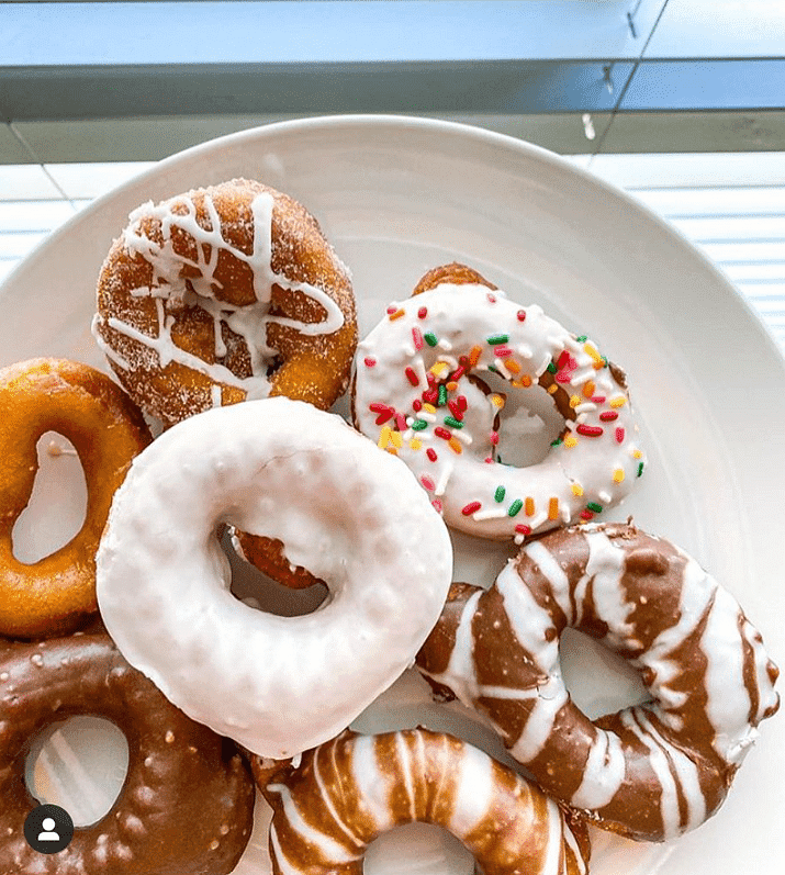 Assorted donuts with various icing and toppings on a white plate, placed near a window.