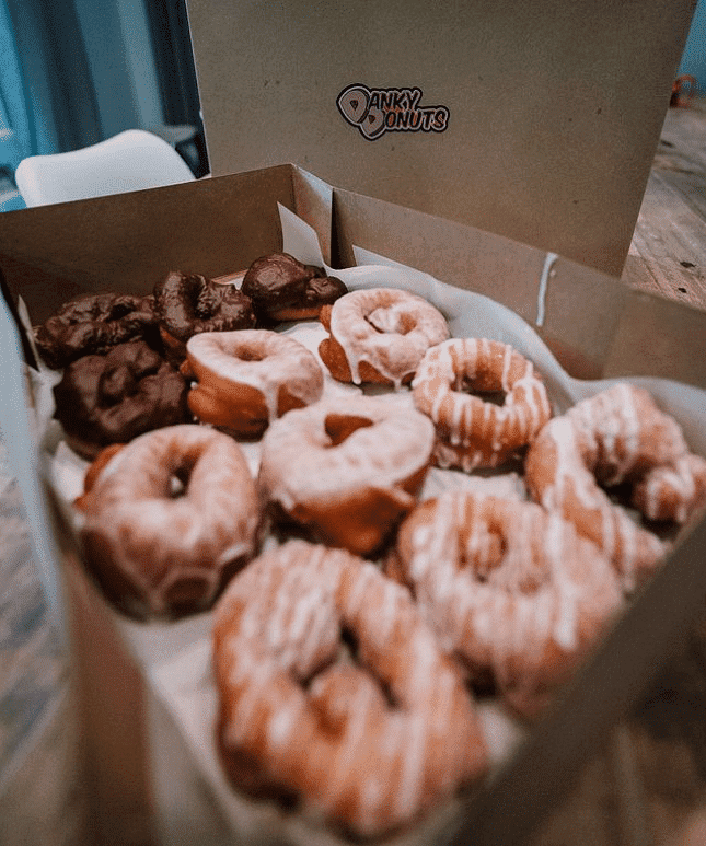 Box of assorted glazed and chocolate donuts from Danky Donuts on a wooden table.