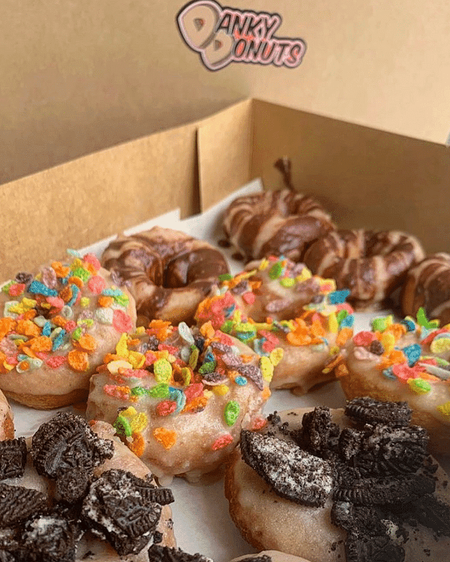 Assorted donuts with colorful toppings in a box from Dandy Donuts.